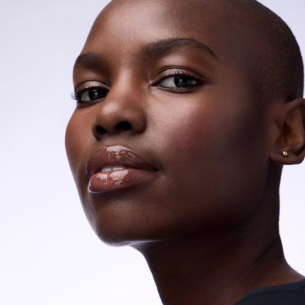 Nahaufnahme einer Frau mit dunkler Haut. Sie hat glänzende Lippen. Blick in die Kamera.
