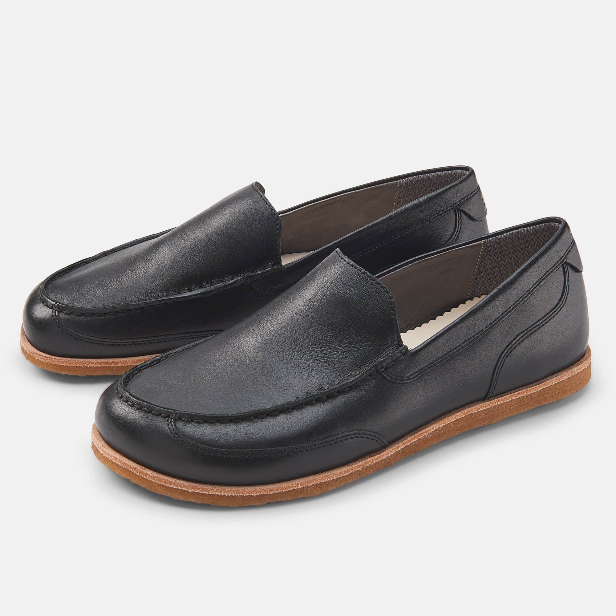 Schwarze Herren-Slipper mit brauner Sohle. Zwei Schuhe nebeneinander, aus Leder. Breite Passform.