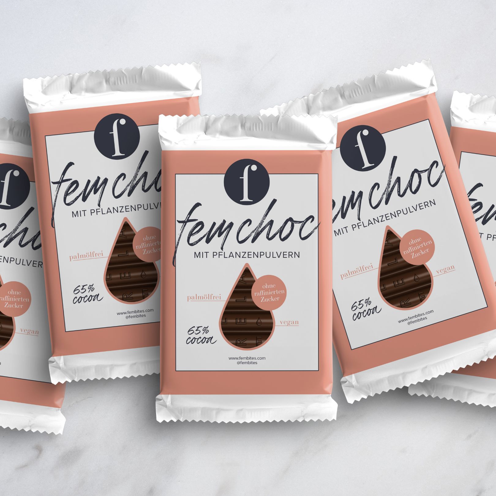 Mehrere verpackte Schokoriegel. Logo und Schriftzug 'fembites femchoc'. Text: 65% Kakao, ohne raffinierten Zucker, vegan.