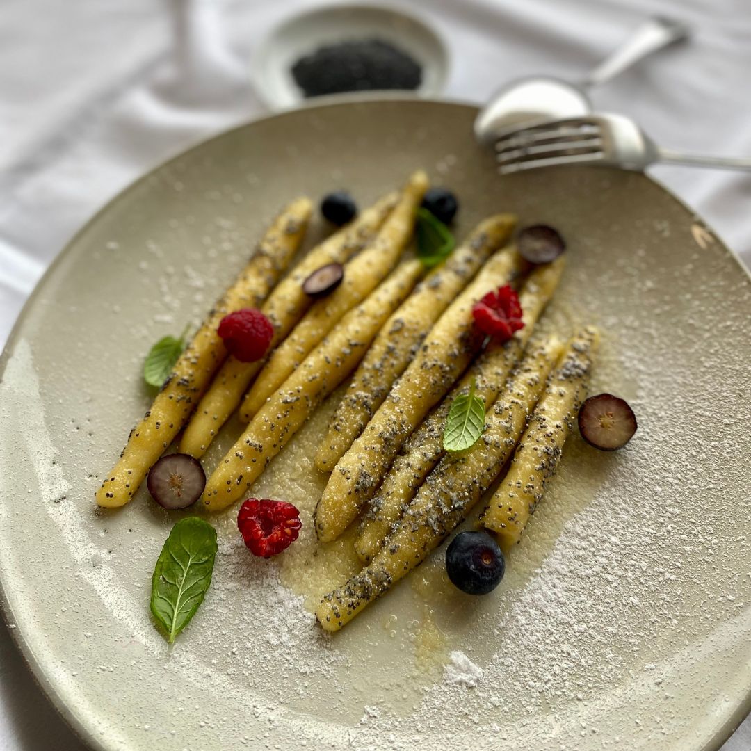 Gnocchi mit Beeren und Minze auf einem Teller. Mit Puderzucker bestreut.