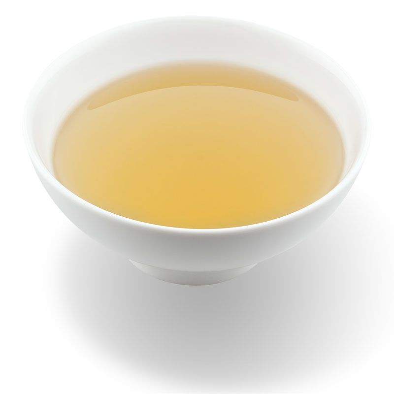 Weiße Schale mit gelbem Tee. Der Tee ist klar und durchsichtig. Die Schale wirft einen Schatten.