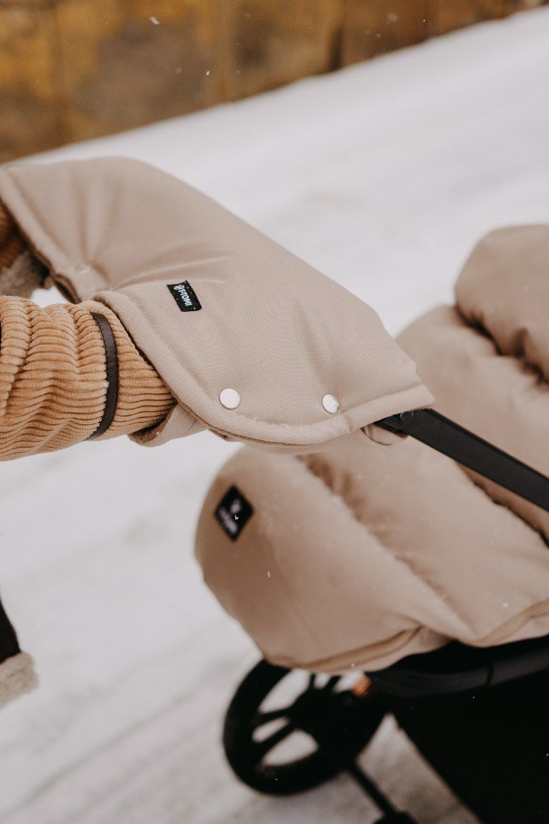 Beige Kinderwagen-Handwärmer aus Stoff mit Druckknöpfen und braunen Lederdetails.