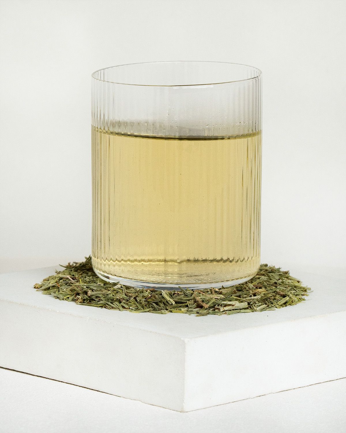 Glas mit Ackerschachtelhalm-Tee und geschnittenem Kraut daneben.