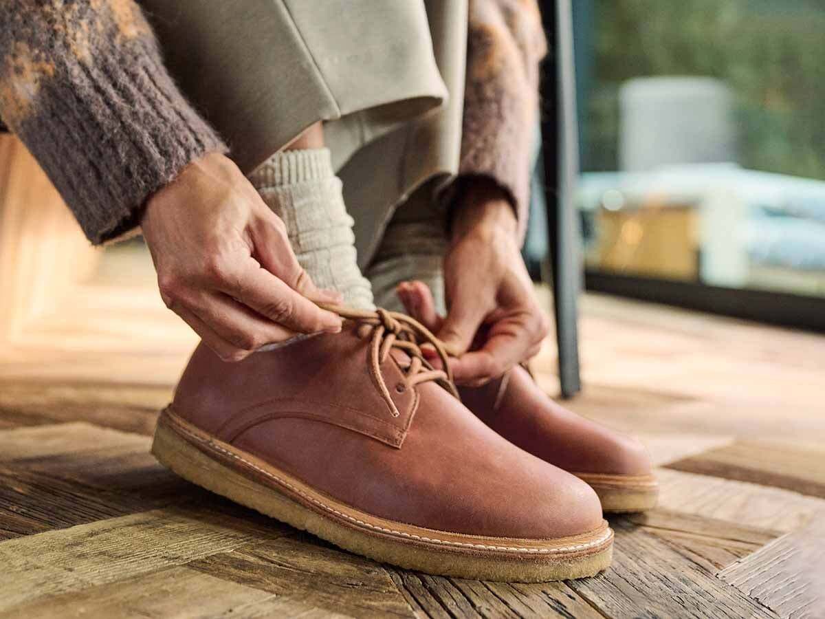 Person bindet braune Lederschnürschuhe mit breiter Sohle. Hellbraune Schnürsenkel. Hellbraune Sohle. Nahaufnahme.