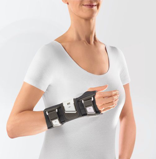 Handgelenkorthese am Handgelenk einer Person. Dunkelgrau mit weißen Elementen und Klettverschlüssen. Das Produkt ist am Handgelenk befestigt.