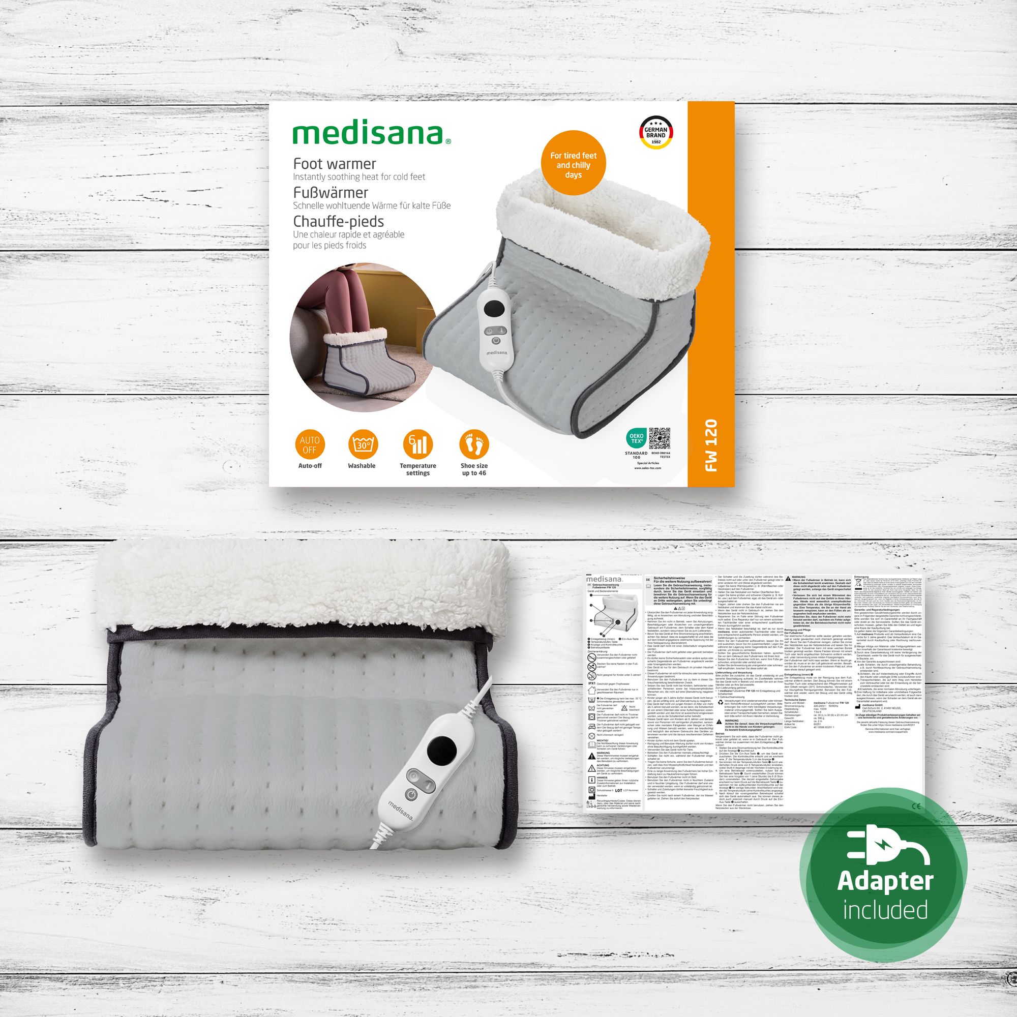 Produktverpackung mit Fußwärmer, Bedienfeld und Zubehör. Text: Adapter Included, FW 120. Das Produkt ist grau mit weißem Innenfutter.