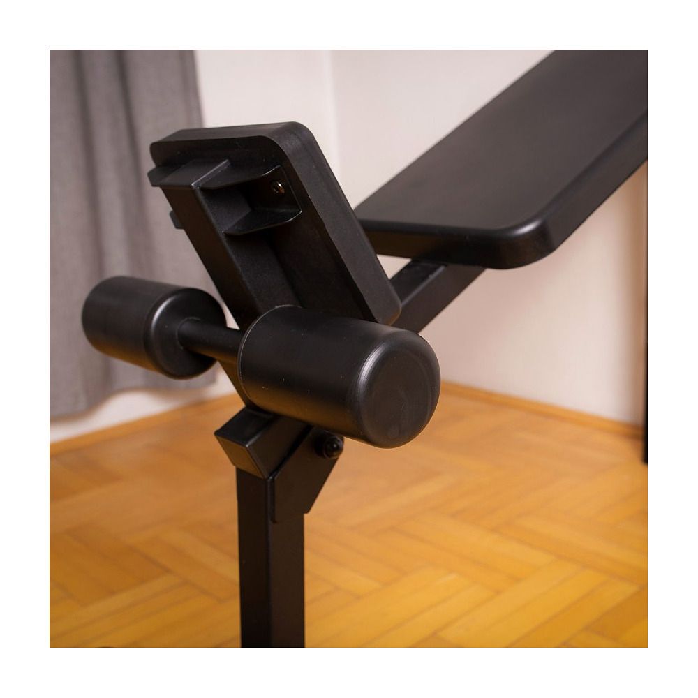 Schwarze Trainingsbank, Seitenansicht. Verstellbare Rückenlehne und Beinpolster. Metallrahmen. Holzfußboden im Hintergrund.