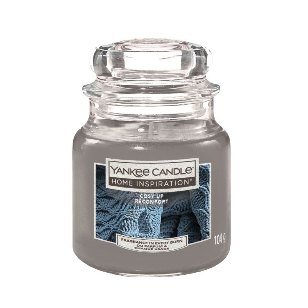 Graue Duftkerze im Glas mit Deckel. Aufkleber mit Schriftzug: Yankee Candle Home Inspiration Cozy Up. 104g.