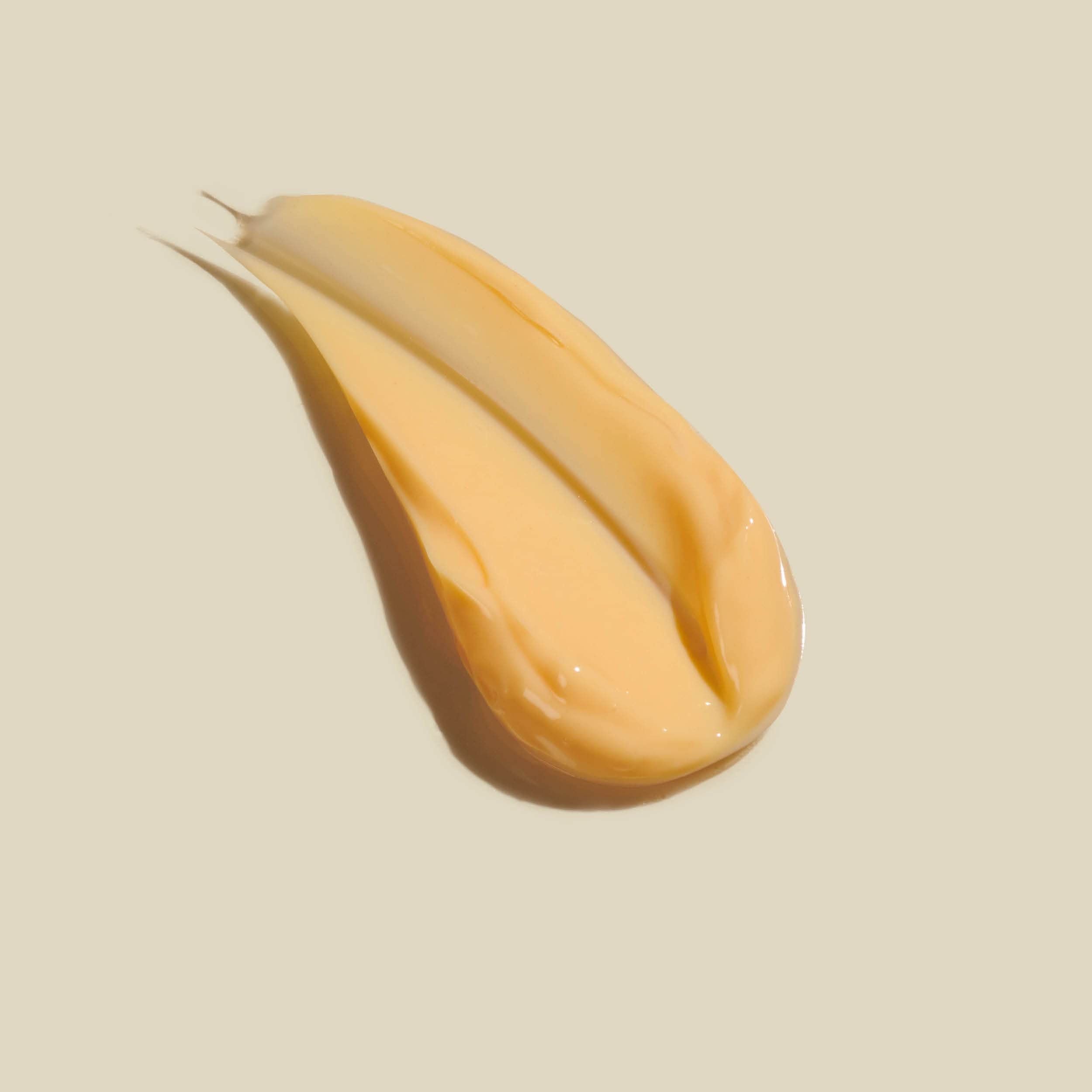 Gelbliche Creme-Spur auf hellem Hintergrund. Die Spur ist länglich und leicht geschwungen.