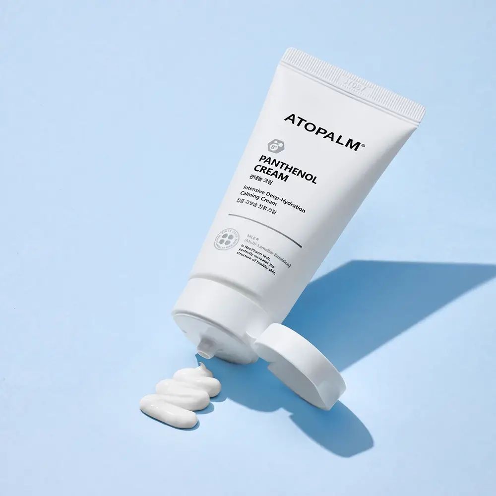 Weiße Tube mit Produktnamen und Logo, mit geöffnetem Deckel und Produkt. Aufschrift: ATOPALM, Panthenol Cream.