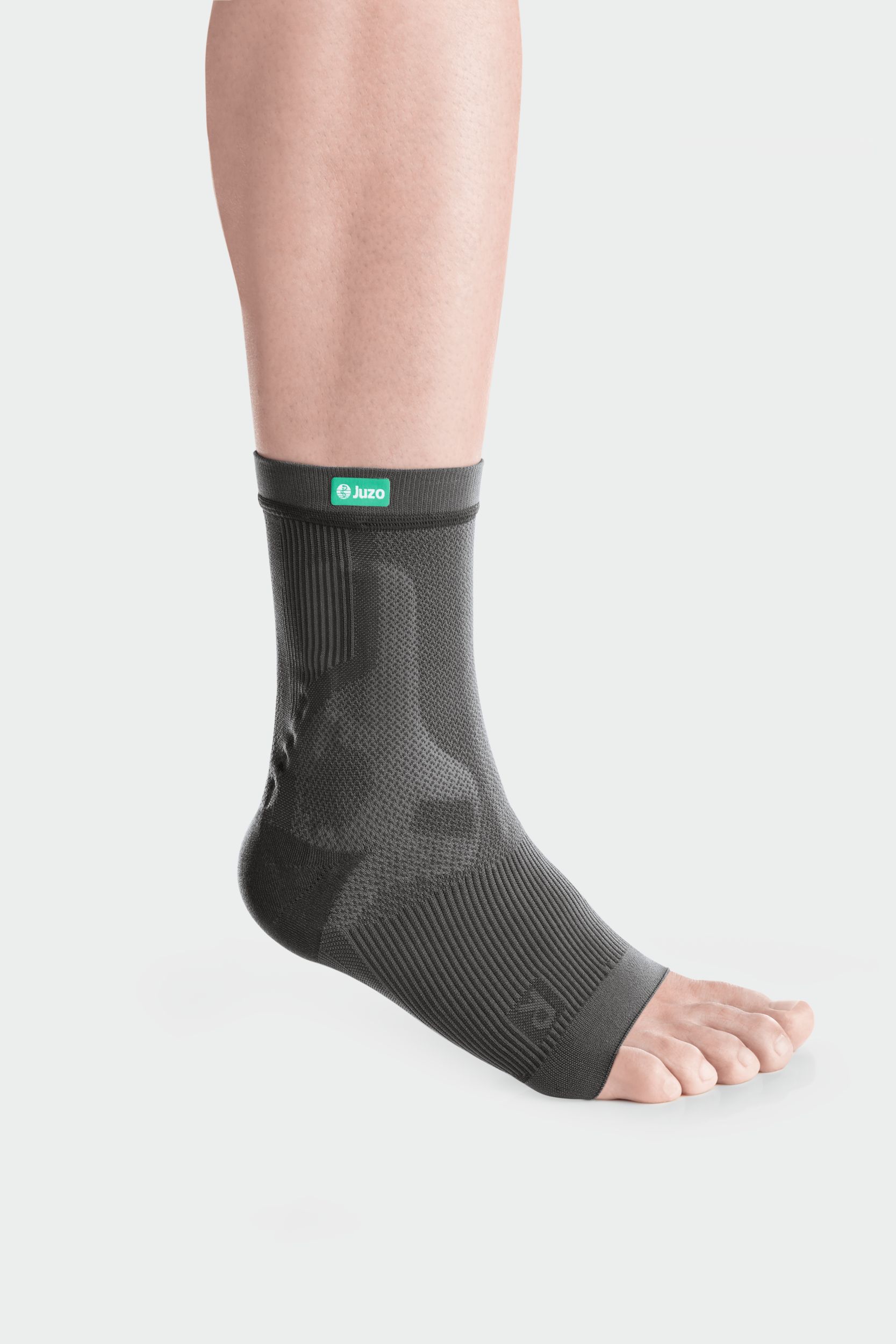 Graue JuzoFlex Malleo Xtra Anatomic Sprunggelenkbandage am Bein. Mit Juzo-Logo. Rippenmuster und anatomische Form.