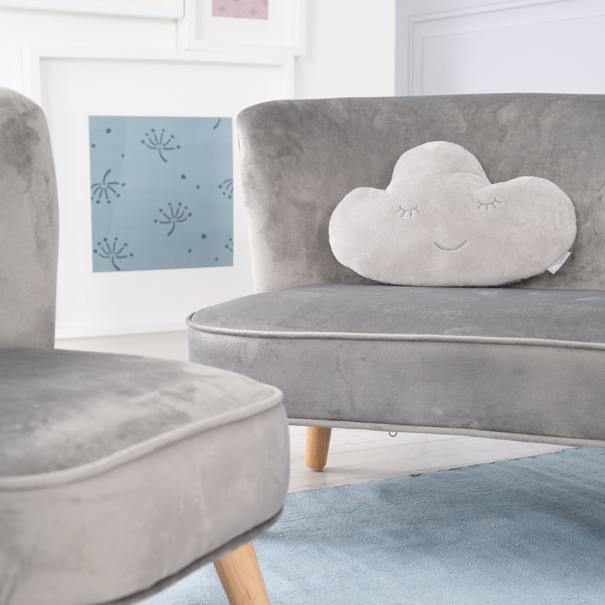 Graues Wolkenkissen auf einem grauen Sofa. Kissen mit geschlossenen Augen und lächelndem Mund. Holzbeine.