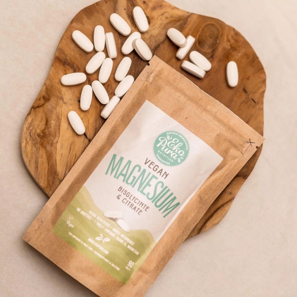 Braune Verpackung mit weißem Etikett. Auf dem Etikett steht "Vegan Magnesium". Daneben liegen Tabletten auf einem Holzbrett.