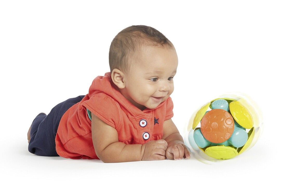 Baby liegt und betrachtet einen bunten Ball. Der Ball hat gelbe, blaue, orange und grüne Elemente. Das Baby trägt einen roten Hoodie.