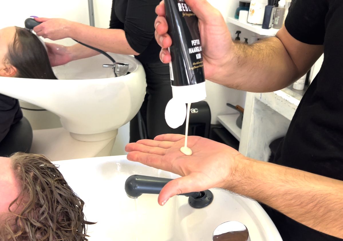 Hand hält schwarze Tube, gibt weiße Flüssigkeit in die Handfläche.