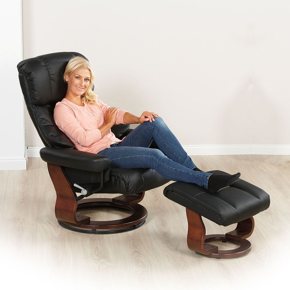 Frau sitzt in schwarzem Relaxsessel mit Hocker. Sie trägt Jeans und ein rosa Oberteil. Holzgestell.