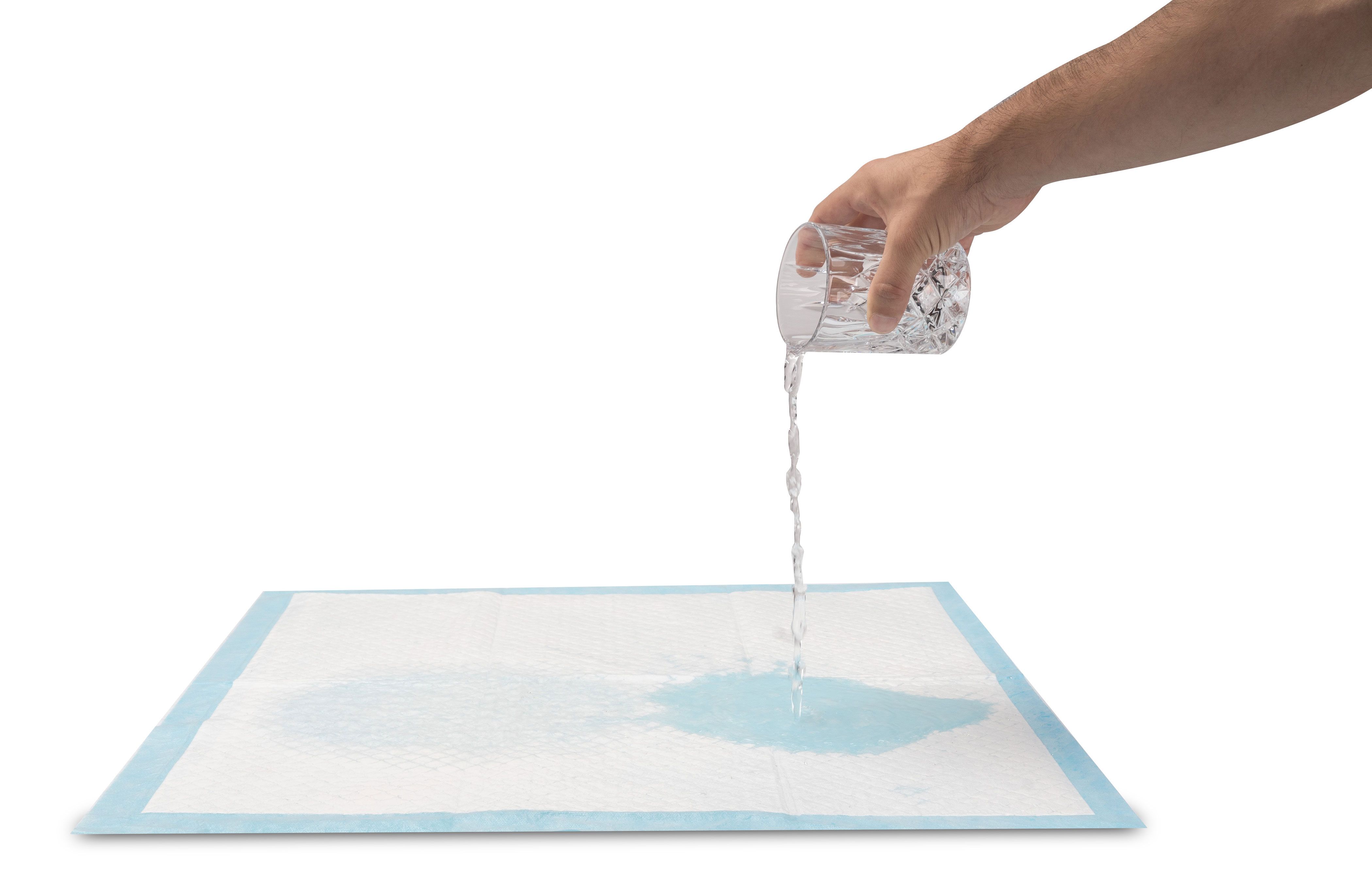 Eine Person gießt Wasser aus einem Glas auf eine Inkontinenz Unterlage. Das Wasser wird absorbiert.