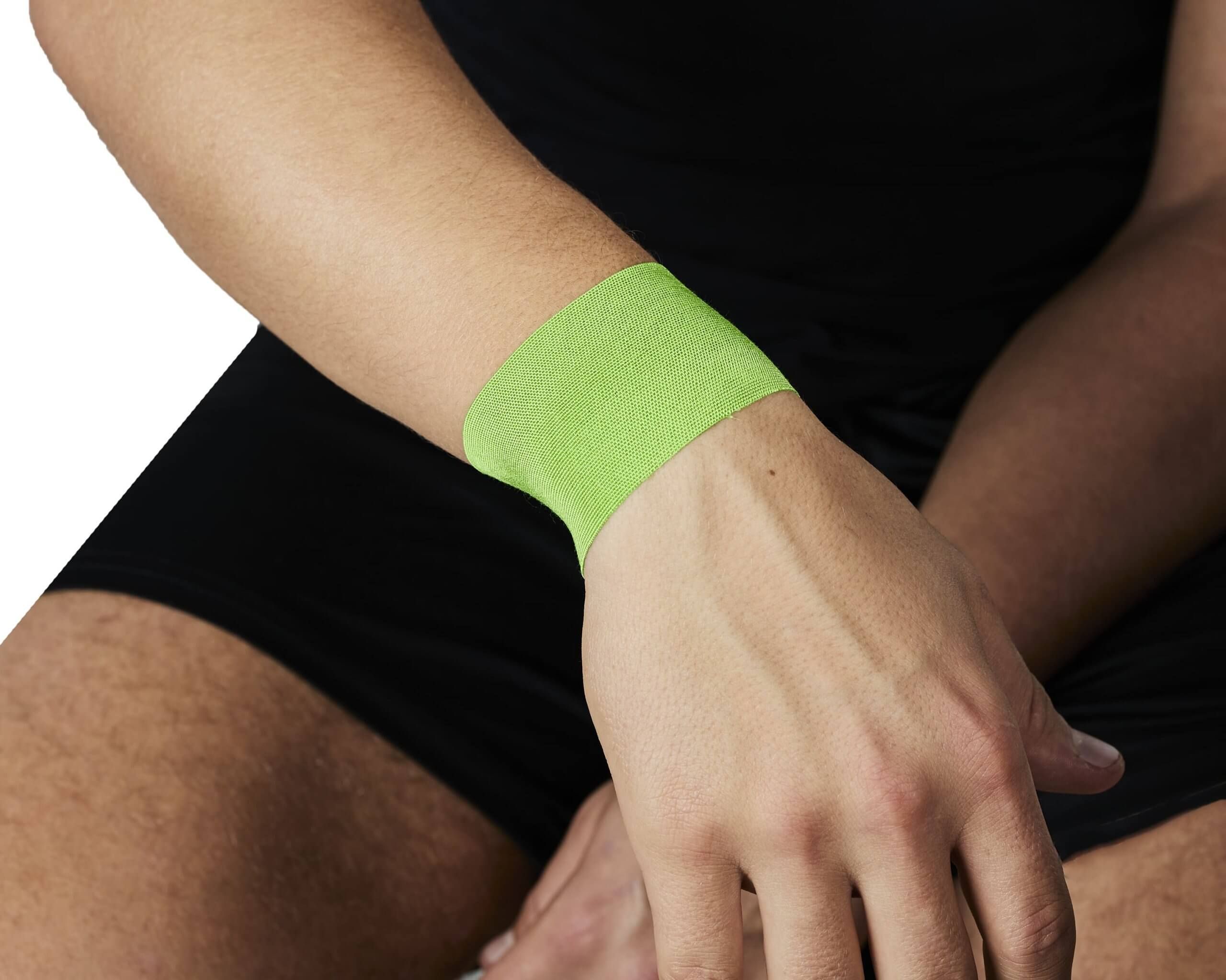 Grünes PhysioTape No.1 am Handgelenk einer Person. Schwarze Kleidung.