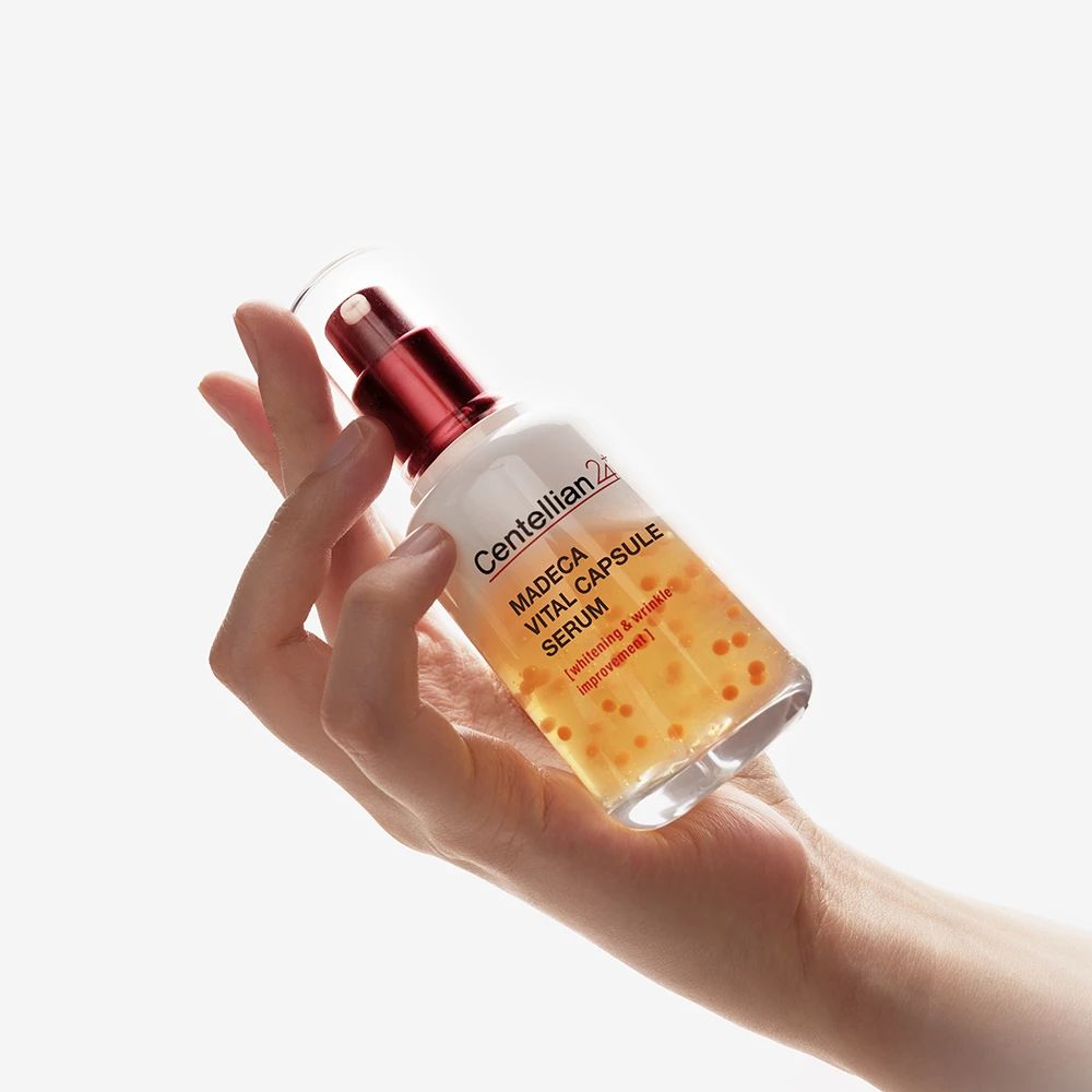 Hand hält Serumflasche. Roter Deckel, transparente Flüssigkeit mit gelben Kügelchen. Flasche leicht geneigt.