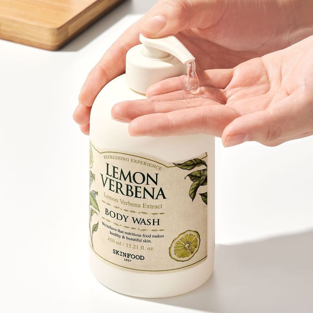Hände drücken Flüssigkeit aus einer "Lemon Verbena" Körperwaschgel-Flasche. Beige Flasche mit Pumpverschluss und Etikett.