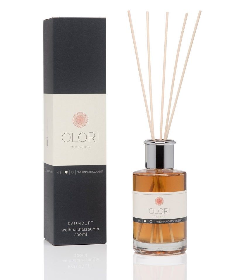 OLORI Reed Weihnachtszauber. Braune Flüssigkeit in Glasflasche mit silbernem Deckel. Schwarze Verpackung mit weißem Etikett und Produktnamen.