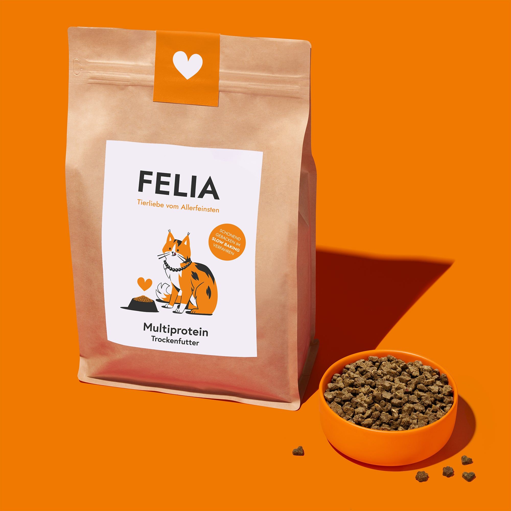Beutel Trockenfutter neben einer Schüssel mit Kroketten. Aufdruck mit Logo, Katze und Text. Orangefarbener Hintergrund.