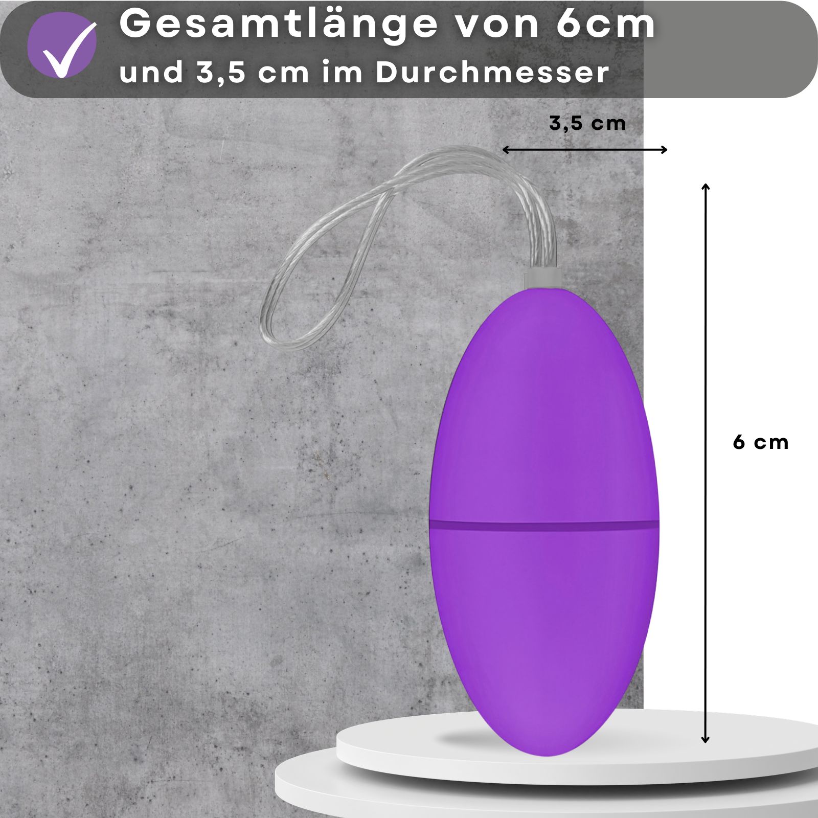 Lila Ei-Vibrator mit Kordel. Abmessungen: 6 cm lang, 3,5 cm Durchmesser. Auf weißem Podest, vor grauer Wand.