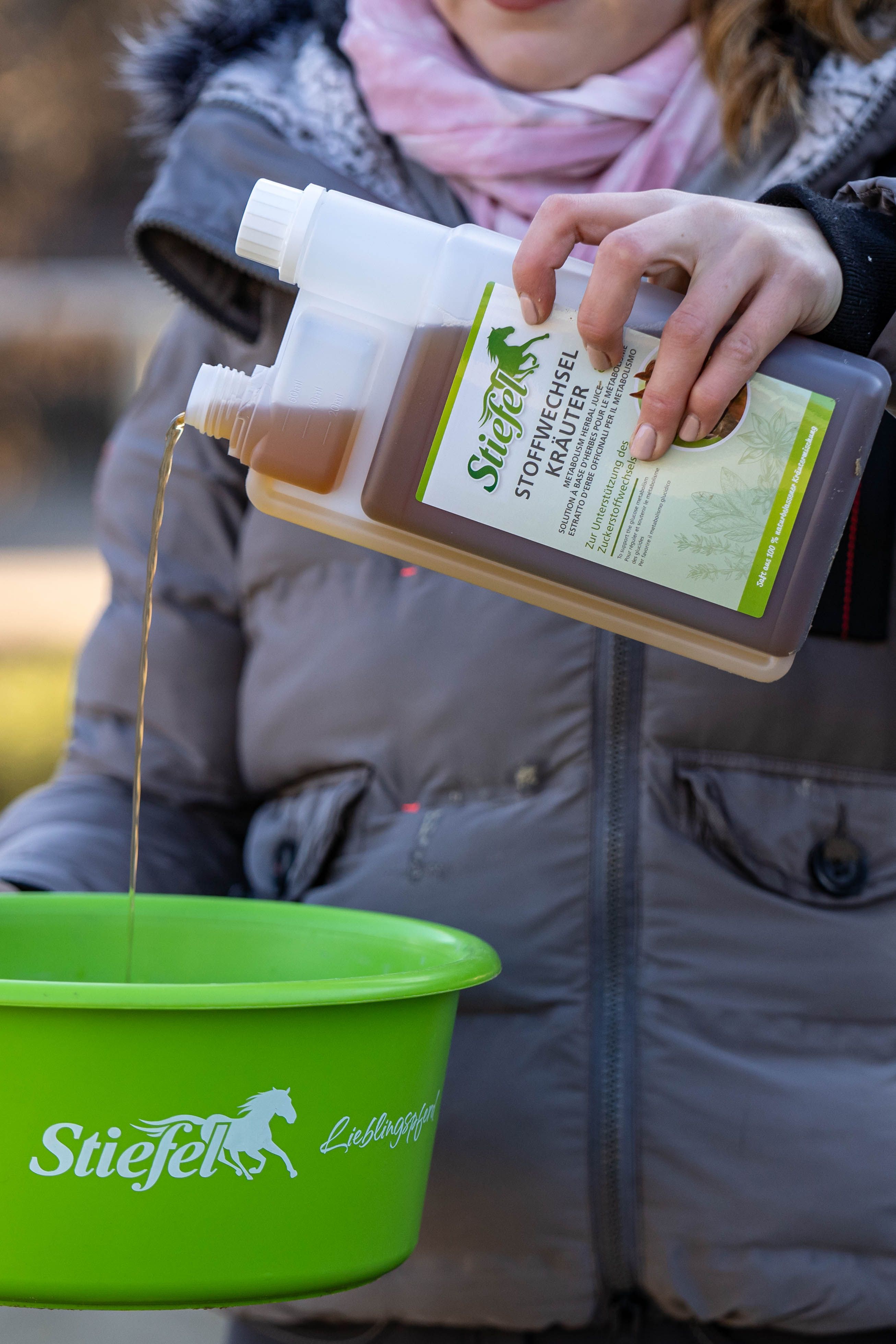 Eine Frau gießt Flüssigkeit aus einer Flasche Stiefel Stoffwechselkräuter in einen grünen Behälter mit Logo.