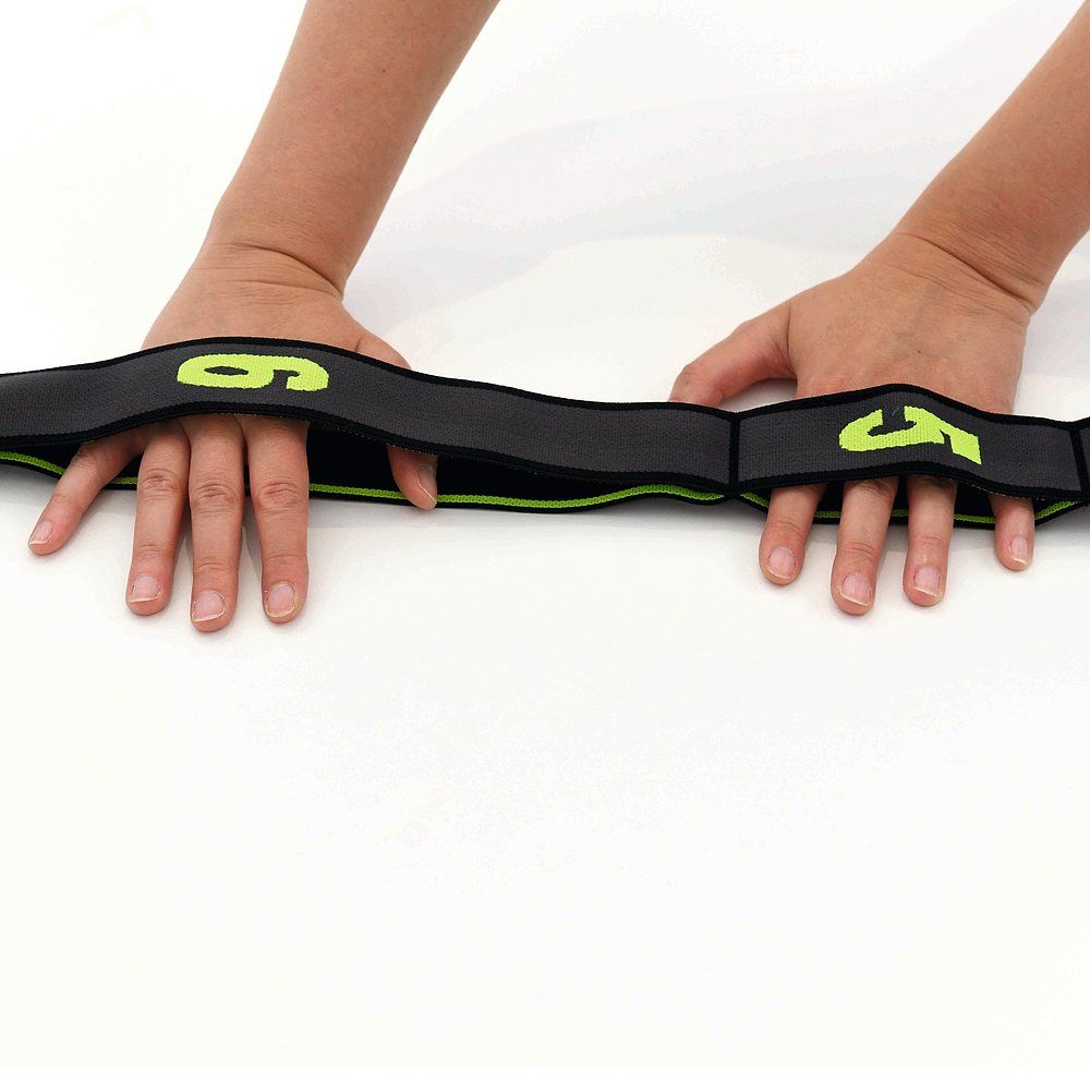 Hände halten ein schwarzes Elastikband mit grünen Markierungen. Zahlen sind sichtbar.