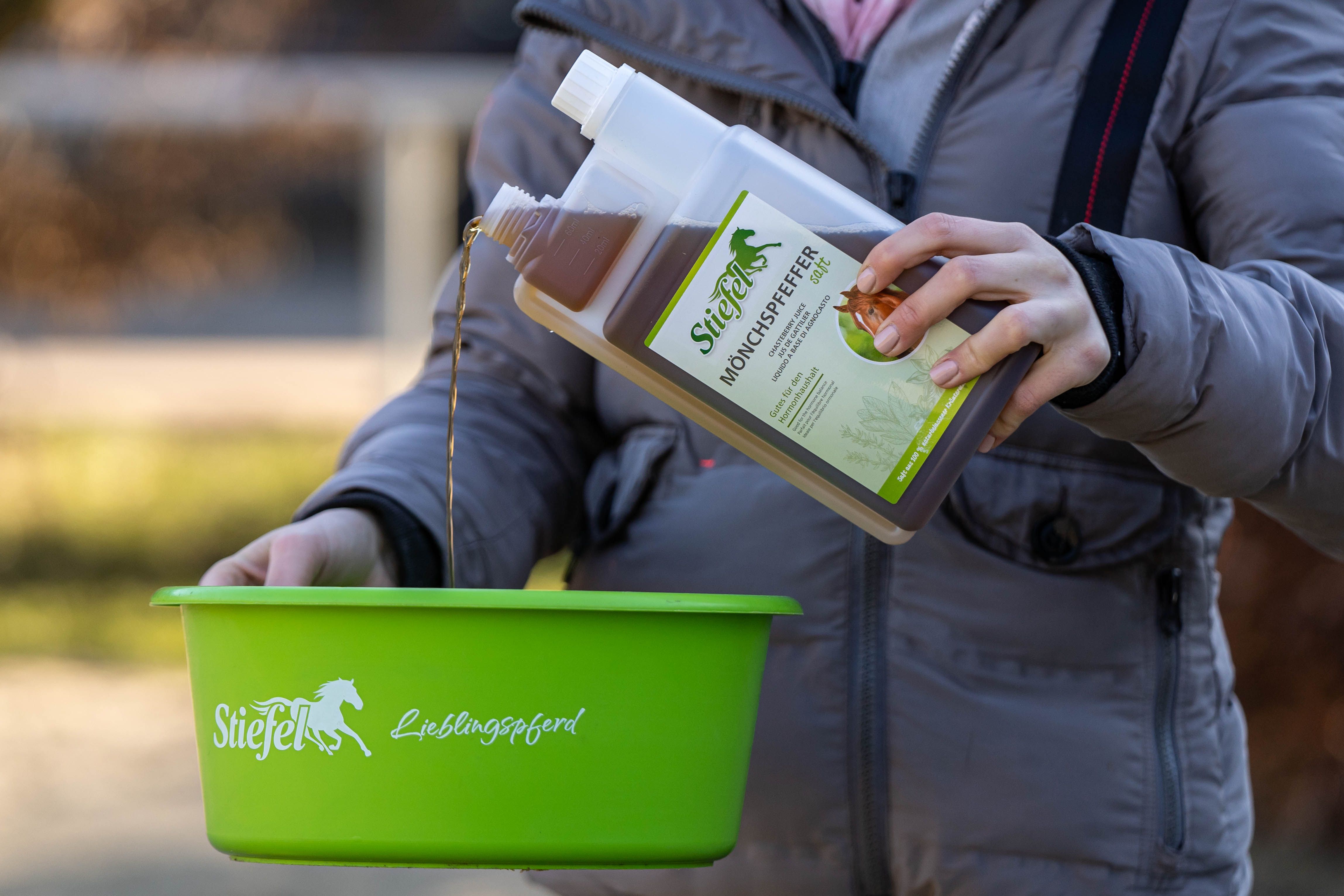 Person gießt braune Flüssigkeit aus einer Flasche Stiefel Mönchspfeffersaft in eine grüne Schüssel.