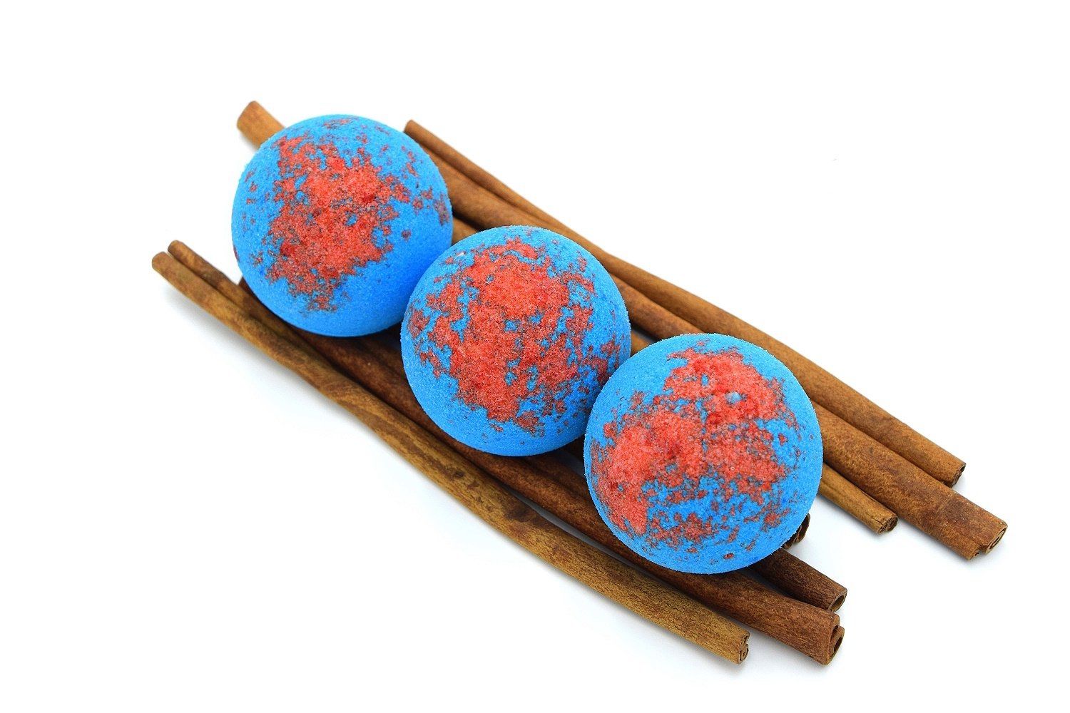 Drei blaue, runde Badebomben mit roter Oberfläche, auf Zimtstangen platziert. Auf weißem Hintergrund.