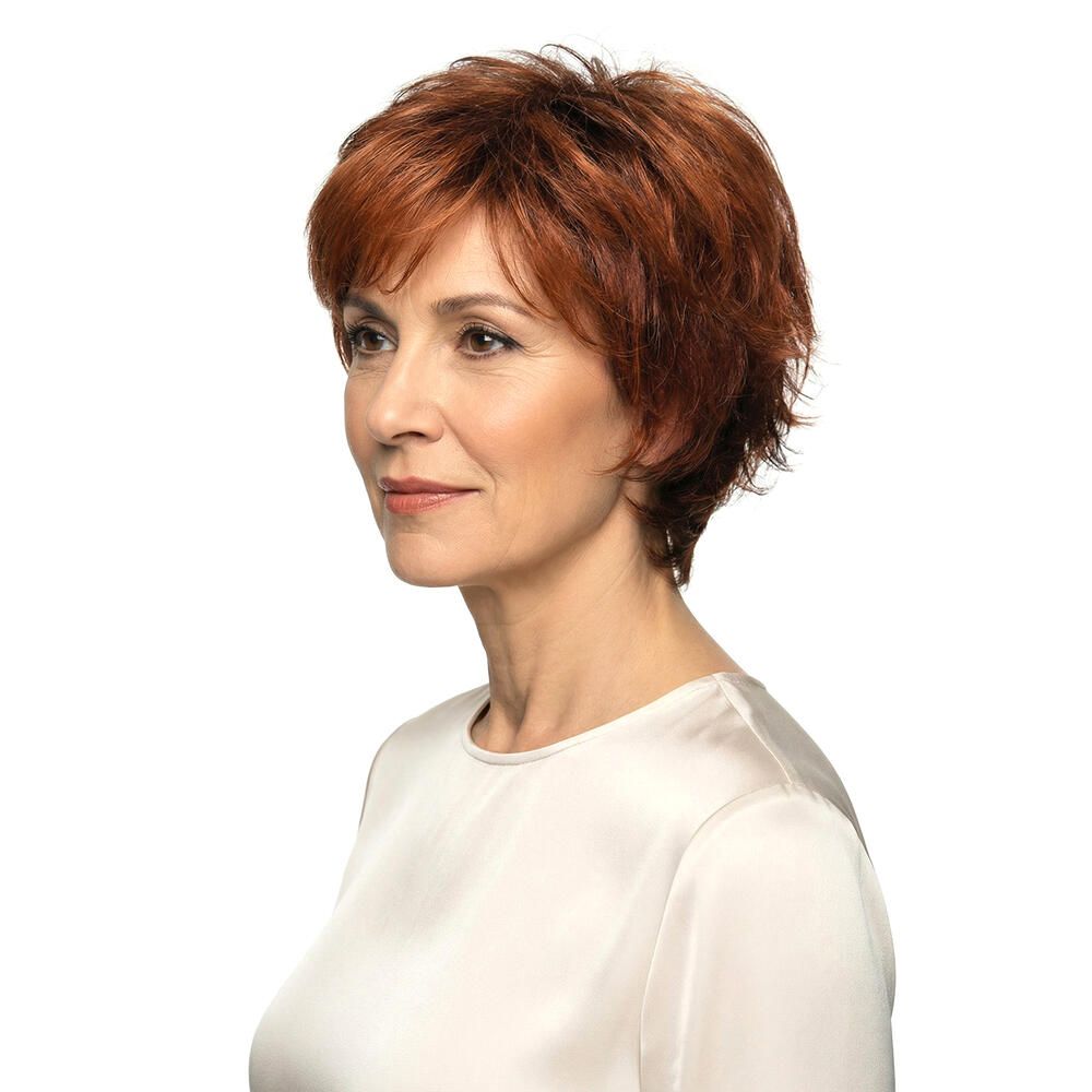 Frau mit rotbrauner Perücke. Seitenansicht. Kurze, gewellte Haare. Helle Haut, weißes Oberteil. Blick zur Seite.