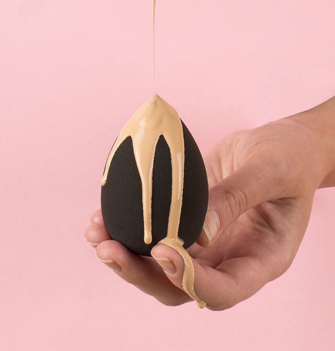 Schwarzer Beauty Blender, von Hand gehalten, mit Make-up-Flüssigkeit bedeckt.