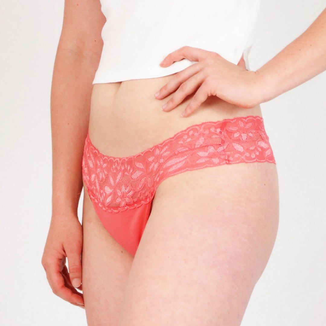 Roter Tanga mit Spitze am Bund. Die Unterwäsche wird von einer Person getragen, die die Hand an die Hüfte legt.