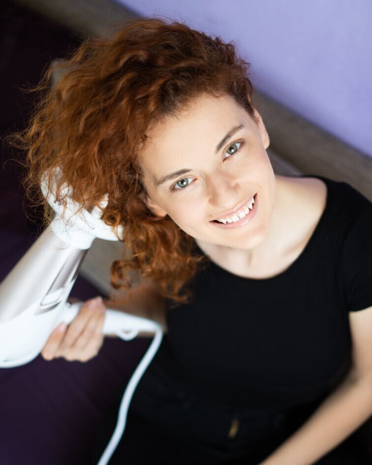 Frau mit lockigem Haar, benutzt einen weißen Haartrockner. Blick von oben.