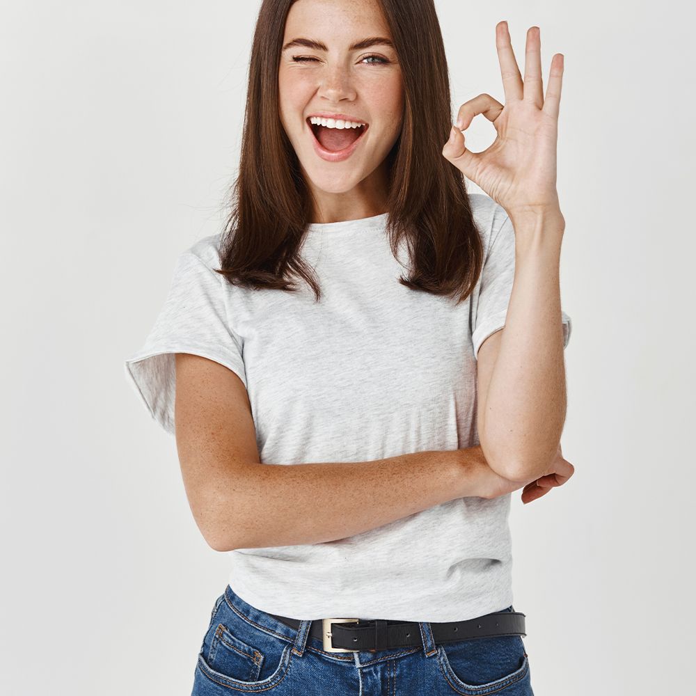Eine Frau mit braunen Haaren und einem grauen T-Shirt. Sie zwinkert und zeigt das 'OK'-Zeichen mit der Hand.