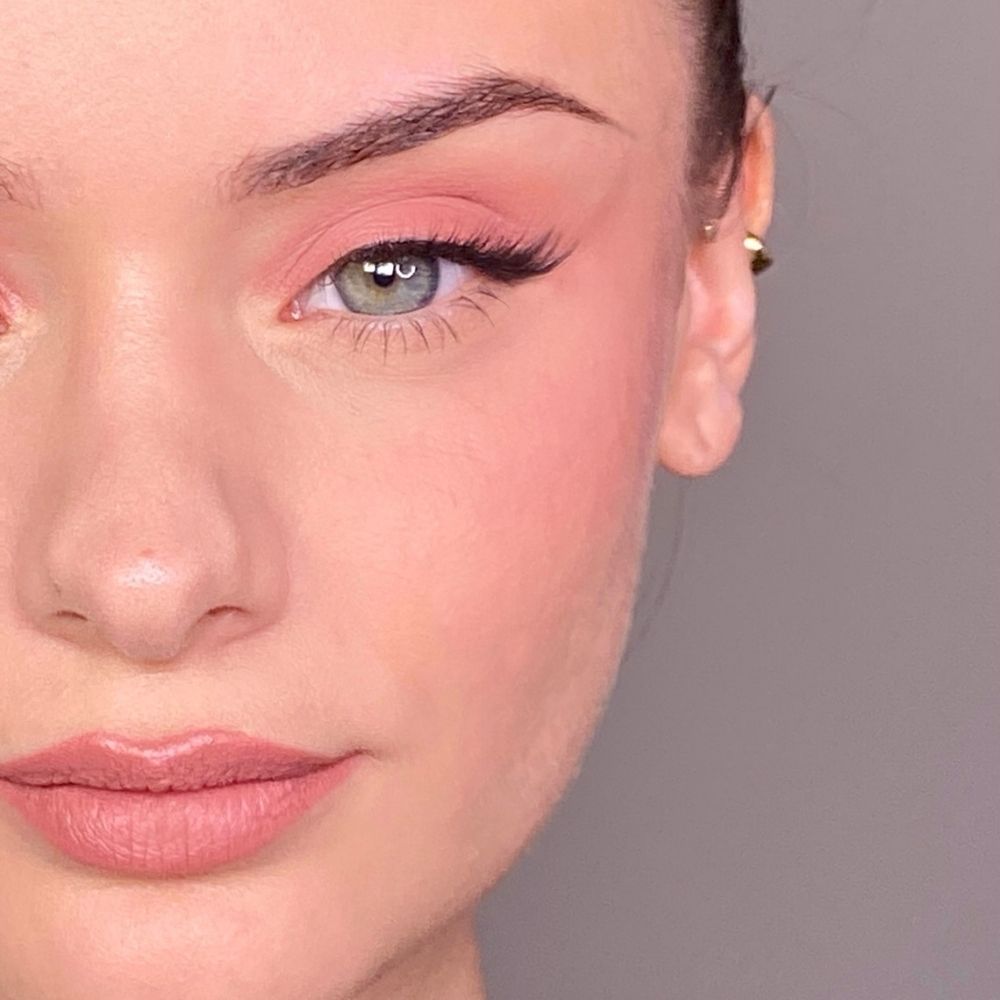 Nahaufnahme eines Gesichts mit rosa Make-up auf Augen und Wangen. Grüne Augen, goldener Ohrring.