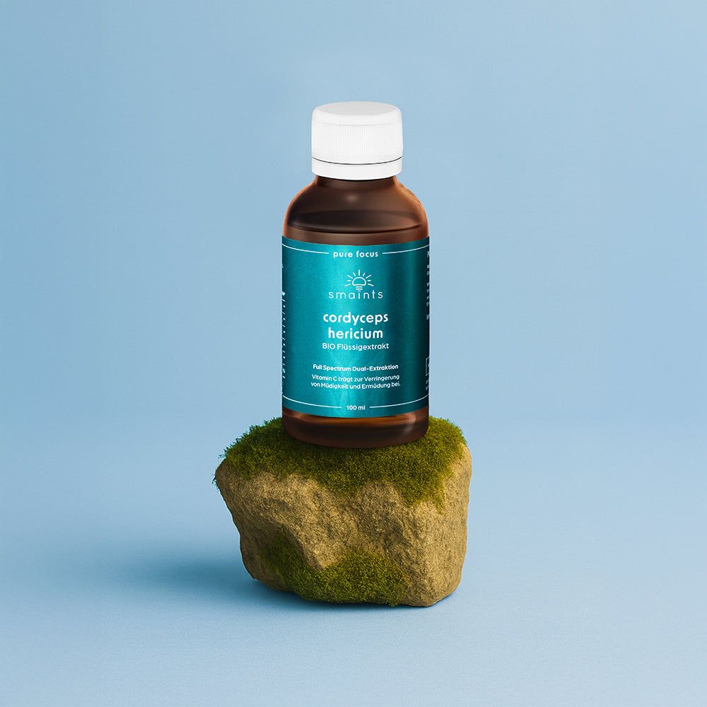 Braune Glasflasche mit weißem Deckel. Türkisfarbenes Etikett. Steht auf einem Stein. Blauer Hintergrund.