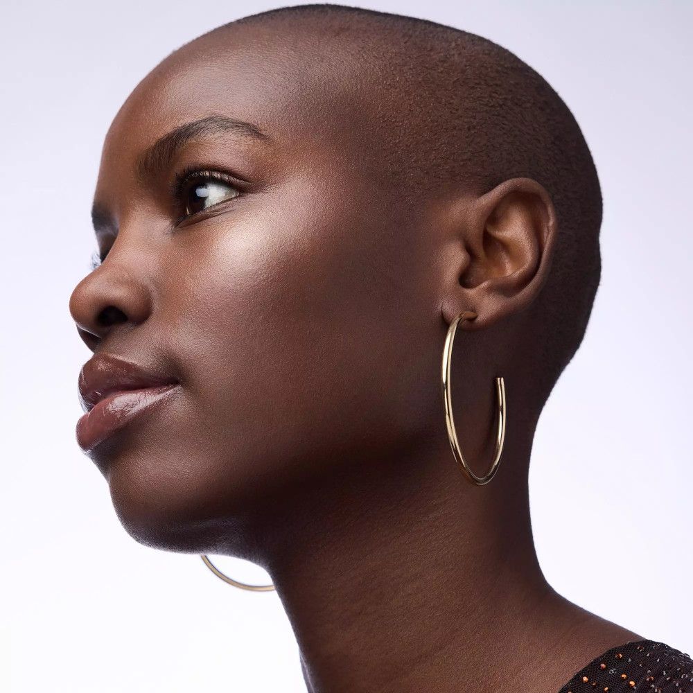 Porträt einer Frau mit dunkler Haut und kurzen Haaren. Sie trägt goldene Creolen.