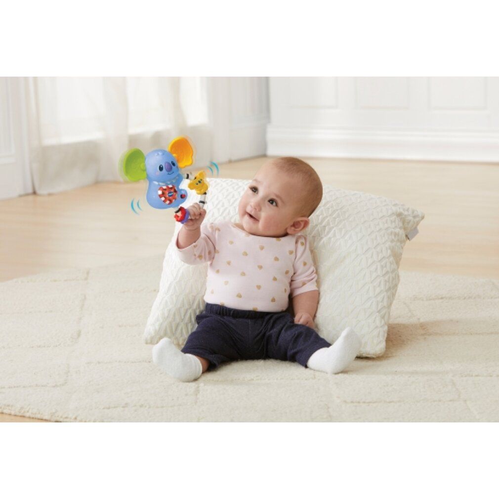 Baby sitzt und spielt mit blauem Koala-Rasselspielzeug. Ring mit bunten Ringen und einem gelben Koala.