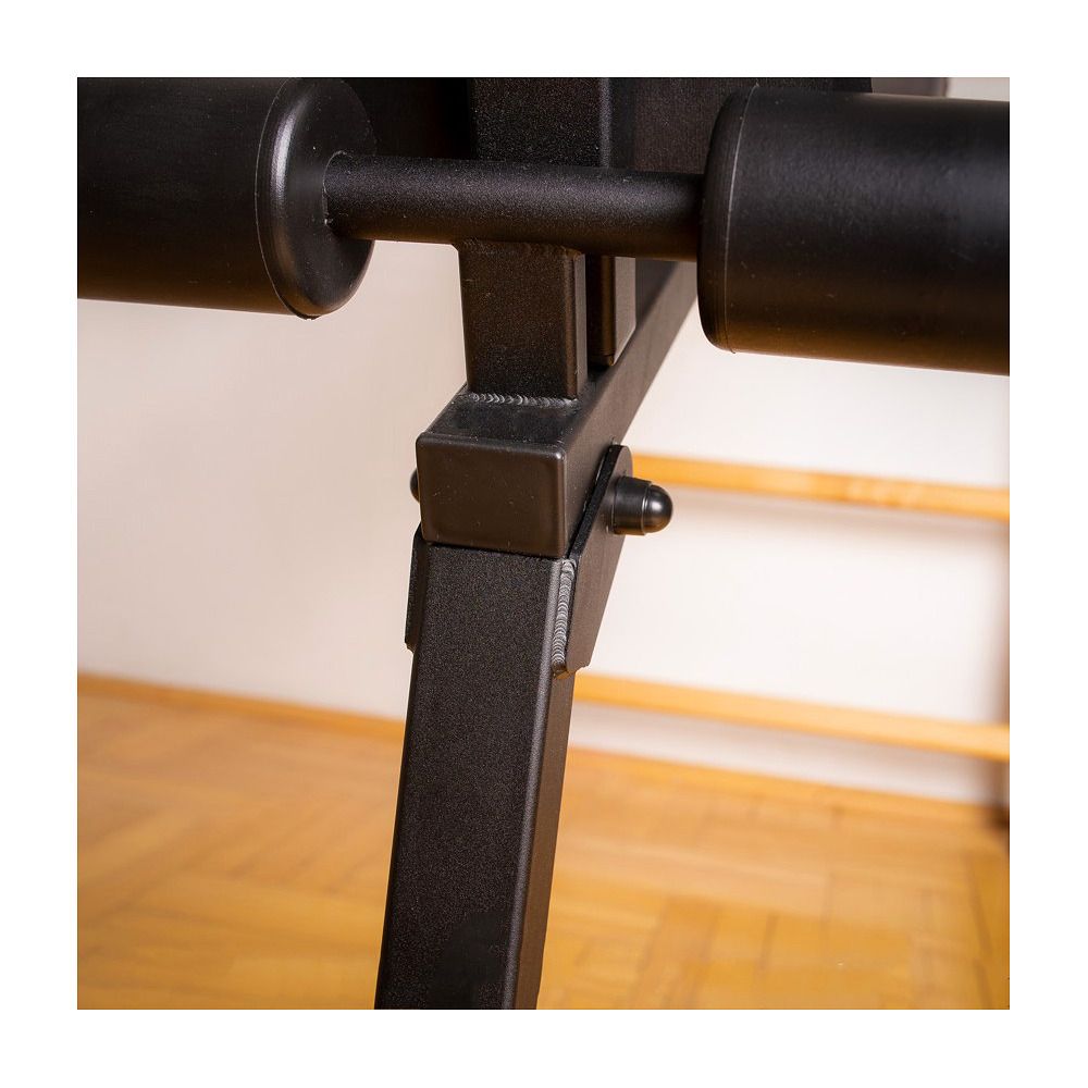 Schwarze Trainingsbank, Detailansicht der Beine und Polster. Metallrahmen mit schwarzen Polstern. Holzfußboden im Hintergrund.