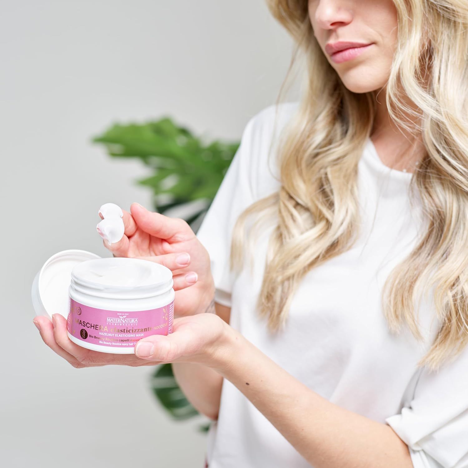 Eine Frau mit blonden Haaren hält einen offenen weißen Tiegel mit Creme.
