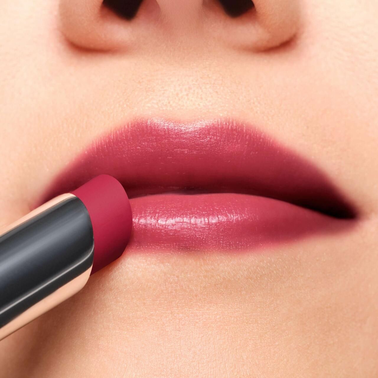 Nahaufnahme von Lippen, die mit einem rosafarbenen Lippenstift geschminkt werden. Der Lippenstift ist in einer silbernen Hülse.