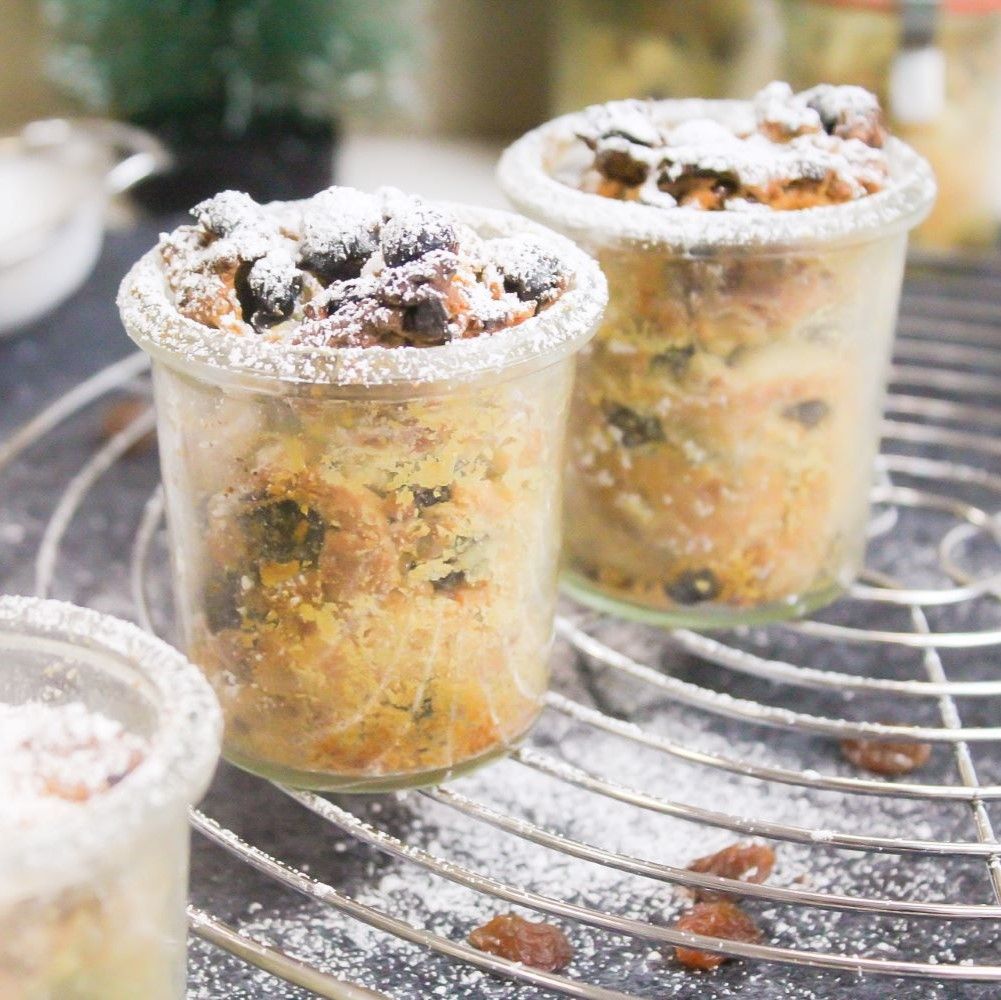 Drei Gläser Christstollen-Dessert auf einem Rost. Mit Puderzucker bestäubt. Rosinen sichtbar.