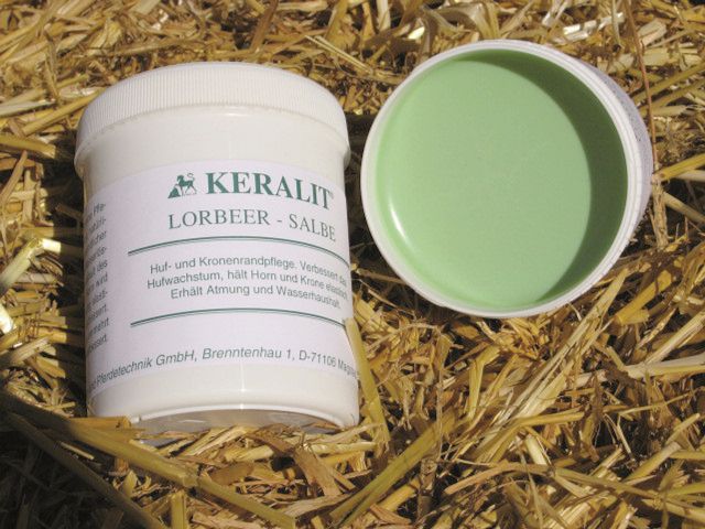 Weißer Tiegel mit Deckel und grüner Salbe. Aufschrift: Keralit Lorbeer-Salbe. Liegt auf Stroh.