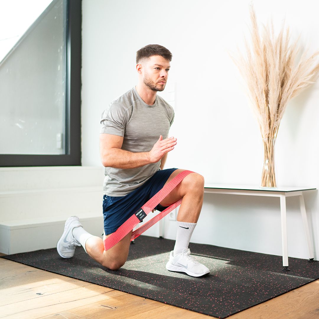 Mann trainiert mit rotem Stoff-Fitnessband. Er kniet auf einer Matte.