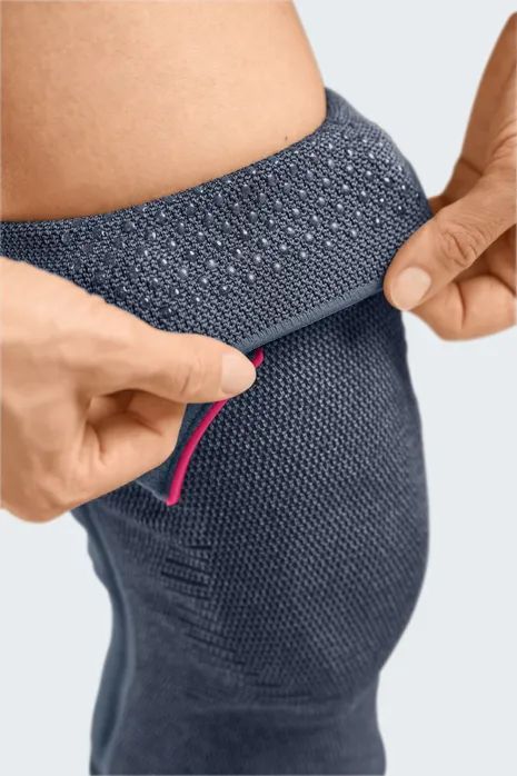 Nahaufnahme einer Knieorthese. Dunkelgraues, gestricktes Material. Hände öffnen einen Klettverschluss.