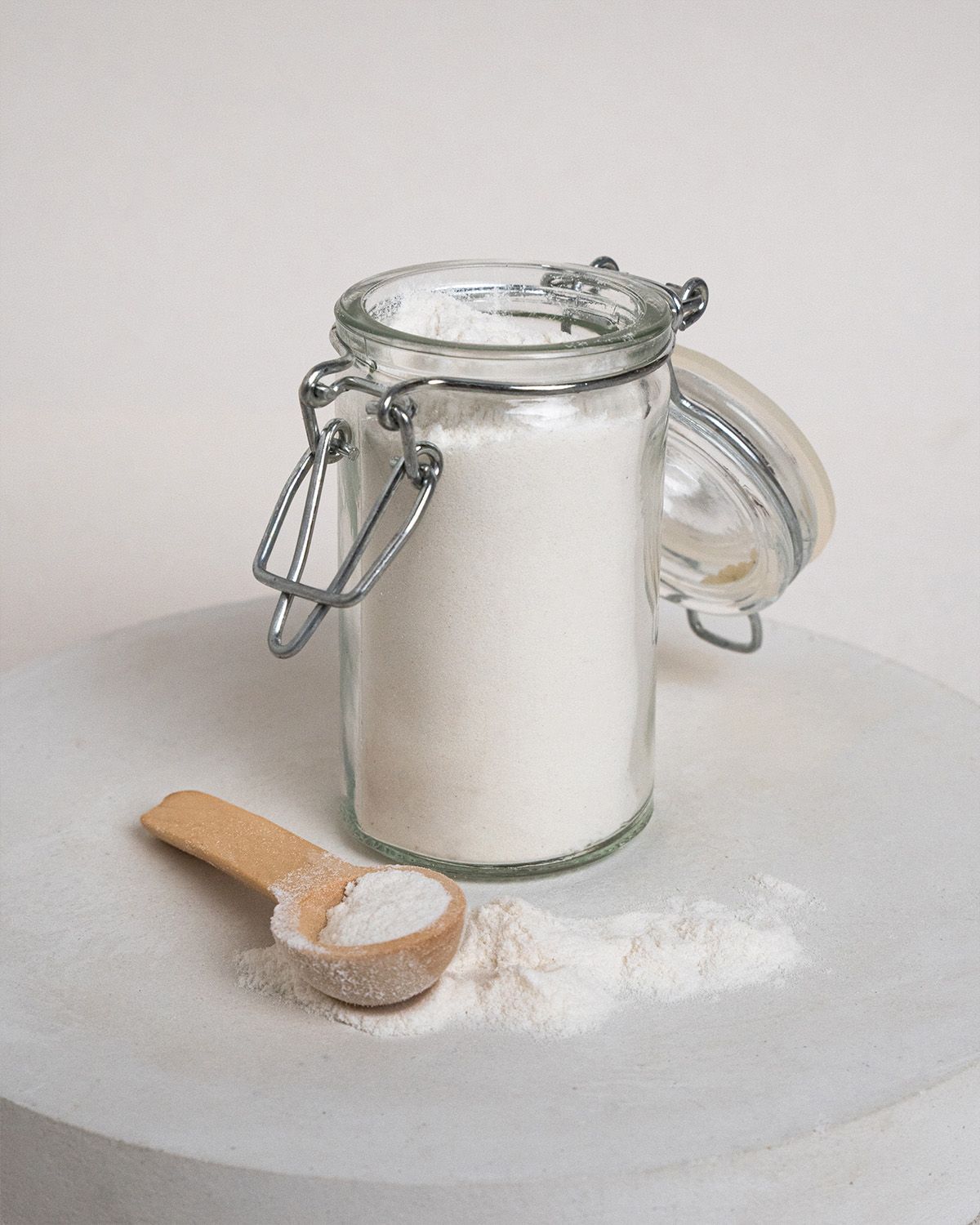 Glasbehälter mit Tarakernmehl, daneben ein Holzlöffel mit Mehl. Deckel geöffnet.