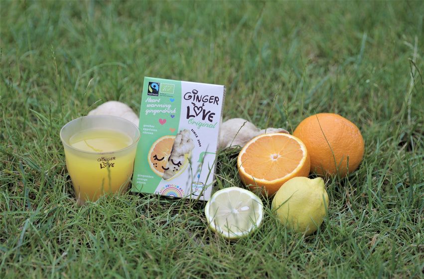 Verpackung mit Text und Illustrationen, daneben ein Glas Saft, Obst auf Gras.