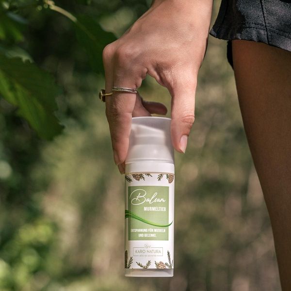 Person hält Balsam-Flasche. Etikett mit Text: Balsam Murmeltier, Karo Natura. Mit Pumpkopf.